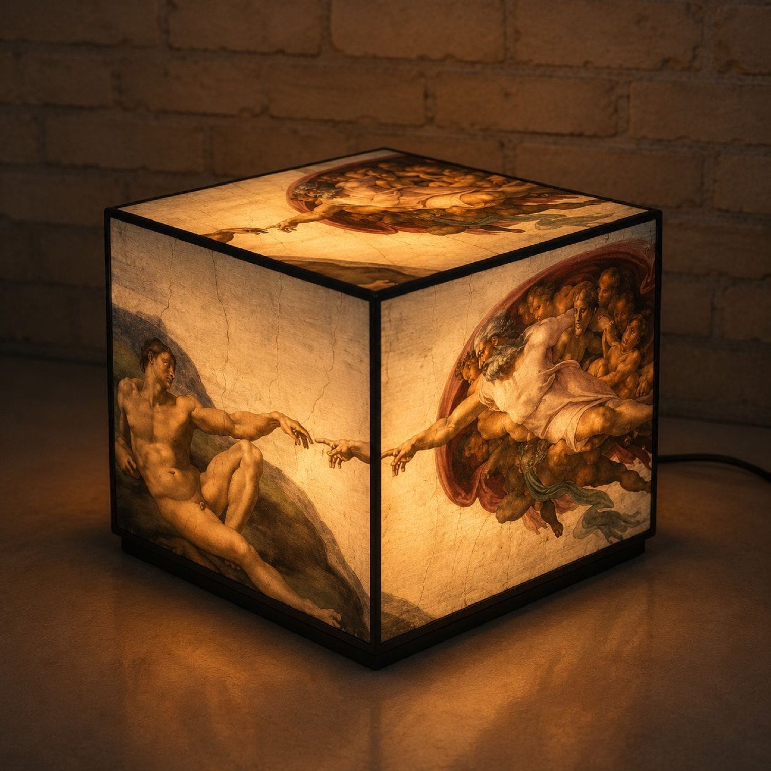 A glowing acrylic lightbox cube wrapped in Michelangelo's Creation of Adam, lit up in a dark brick-walled room